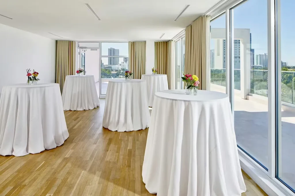 Bright modern event space with high-top tables, flowers, and city view.