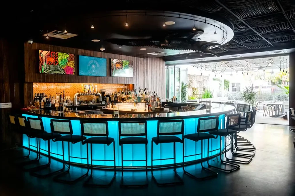 Modern bar with aqua-lit counter, liquor display, and outdoor patio.