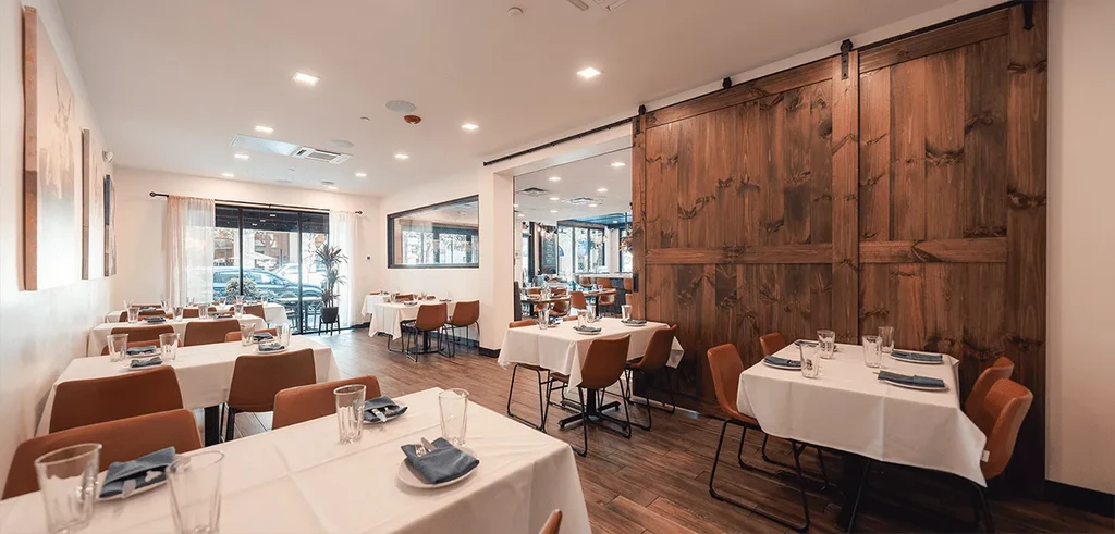 Empty, modern restaurant dining room with set tables and a barn door.