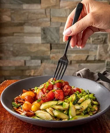 Hand holding fork taking a bite from a colorful poke bowl.