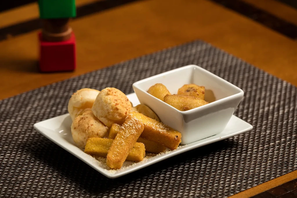 White plate holds golden-brown fried appetizers, including cheese bread and fries.