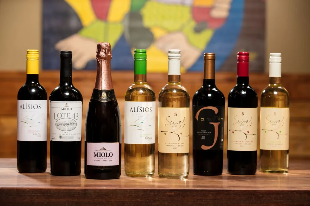 Eight wine and sparkling wine bottles lined up on a dark wooden surface.