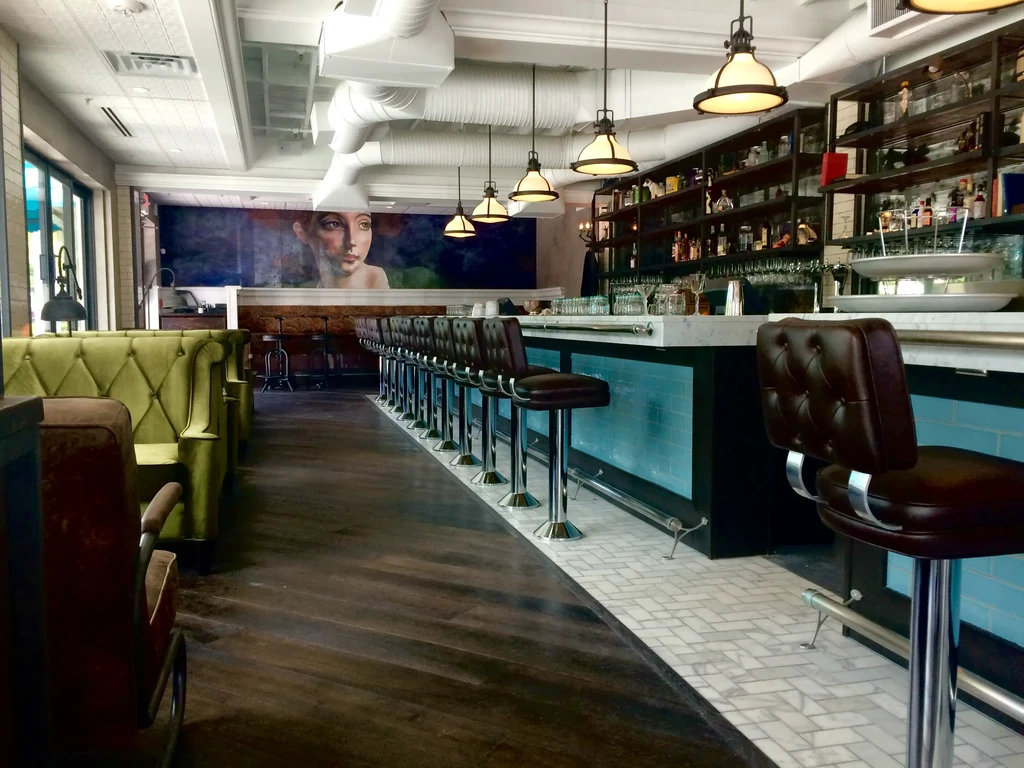 Stylish bar interior with marble counter, green booths, and woman's mural.