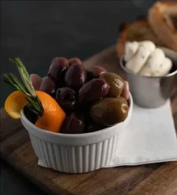 White bowl of olives, orange peel, rosemary, butter, and toast.