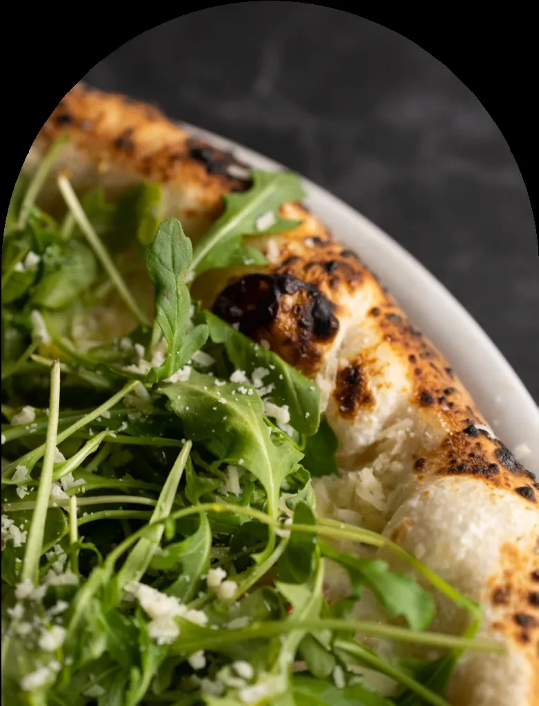 Blistered flatbread pizza topped with fresh arugula and grated cheese.