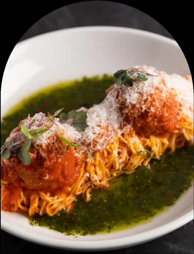 Spaghetti and meatballs with marinara, Parmesan, microgreens, and green sauce.