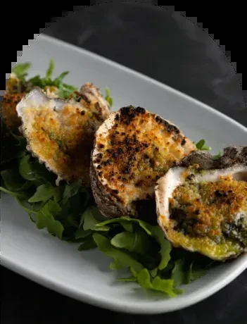 Four baked oysters with golden topping on fresh green leaves.