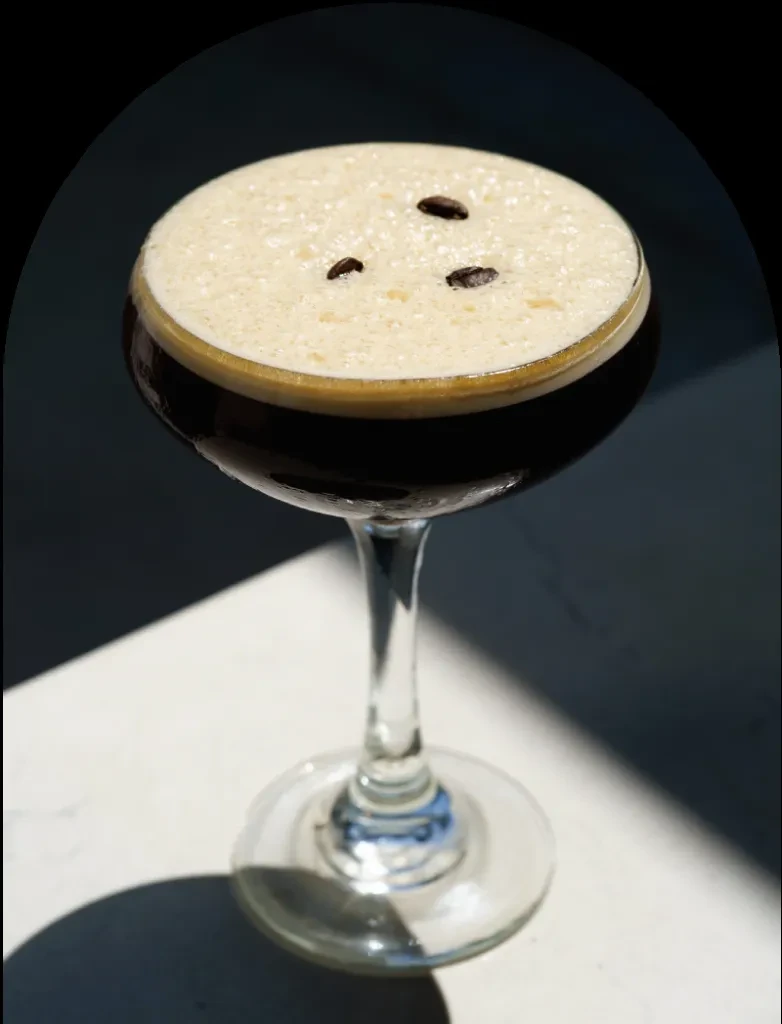 Close-up of espresso martini with thick foam and three coffee beans.