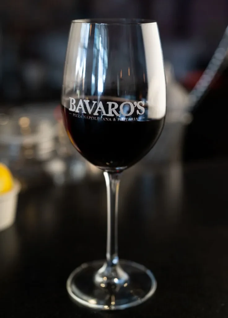 Red wine glass with BAVARO'S logo on a dark, reflective surface.