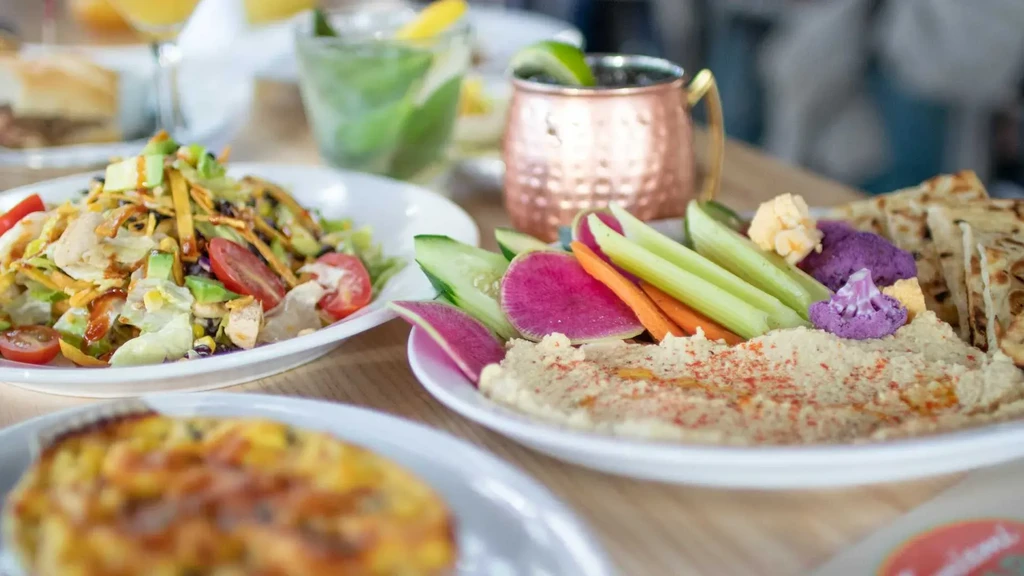 Hummus with crudités, salad, savory tart, and drinks on a table.