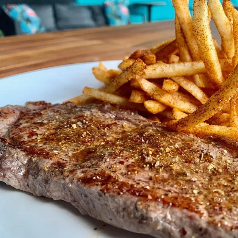 Grilled steak and heavily seasoned golden fries on a white plate.