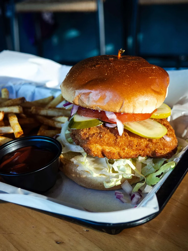 Crispy fried chicken sandwich with toppings, fries, and dipping sauce.