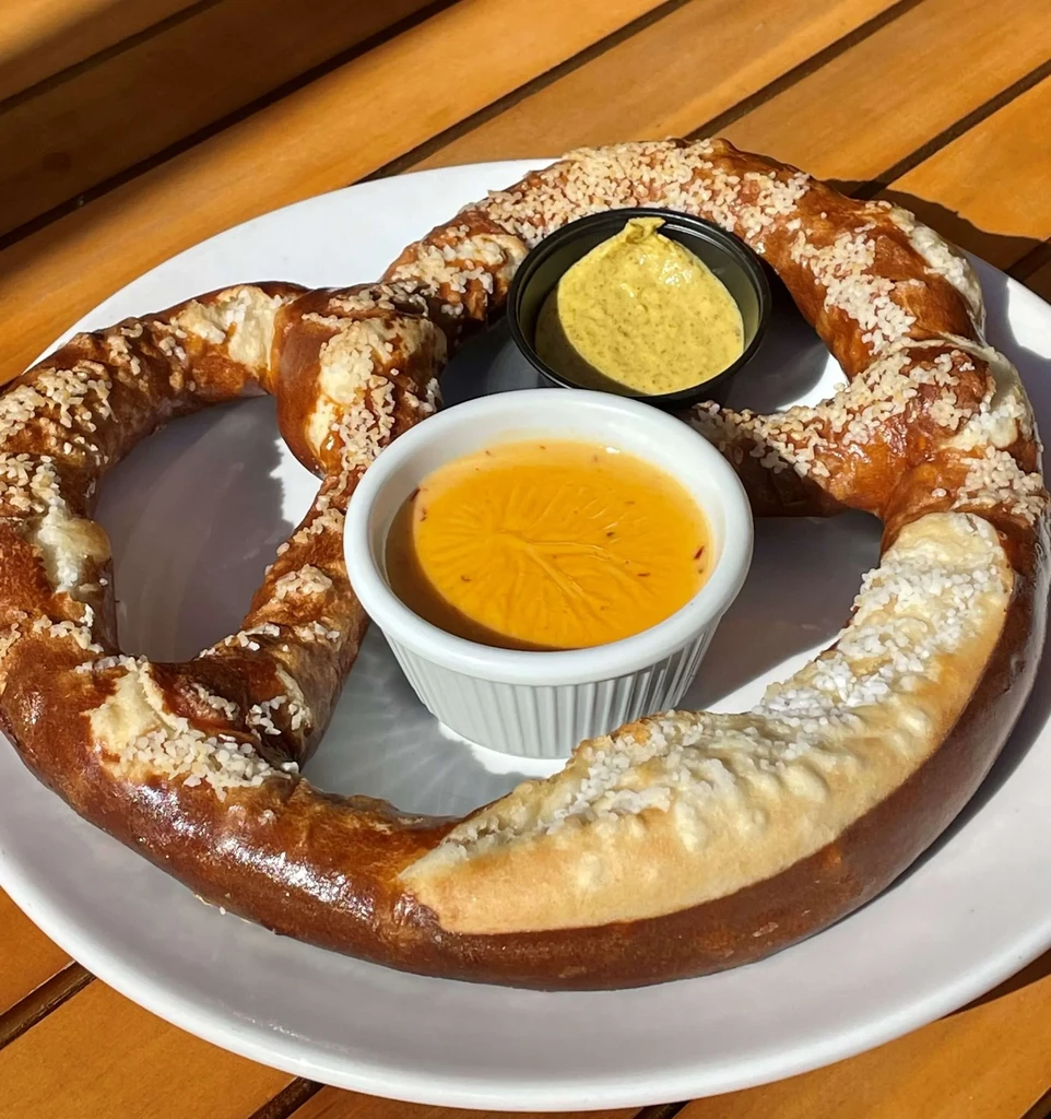 Large, salted pretzel on a white plate with two dipping sauces.