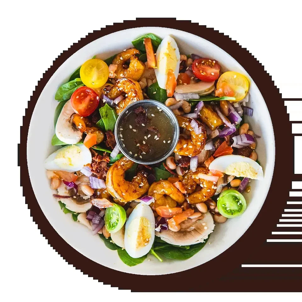 Top-down view of a salad with shrimp, eggs, tomatoes, greens, and dressing.