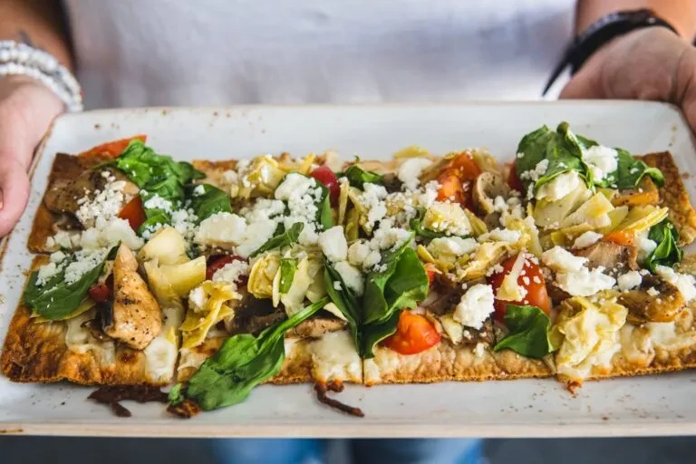 Rectangular flatbread pizza topped with chicken, spinach, tomatoes, and feta cheese.