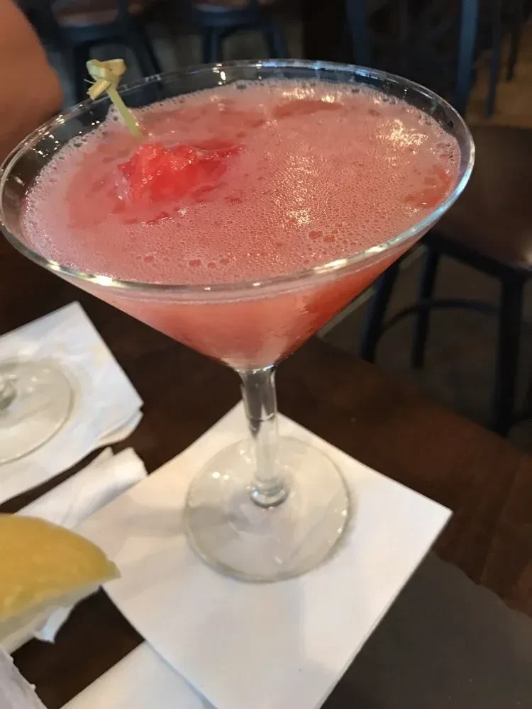 Frothy pink cocktail in martini glass with red fruit on dark table.