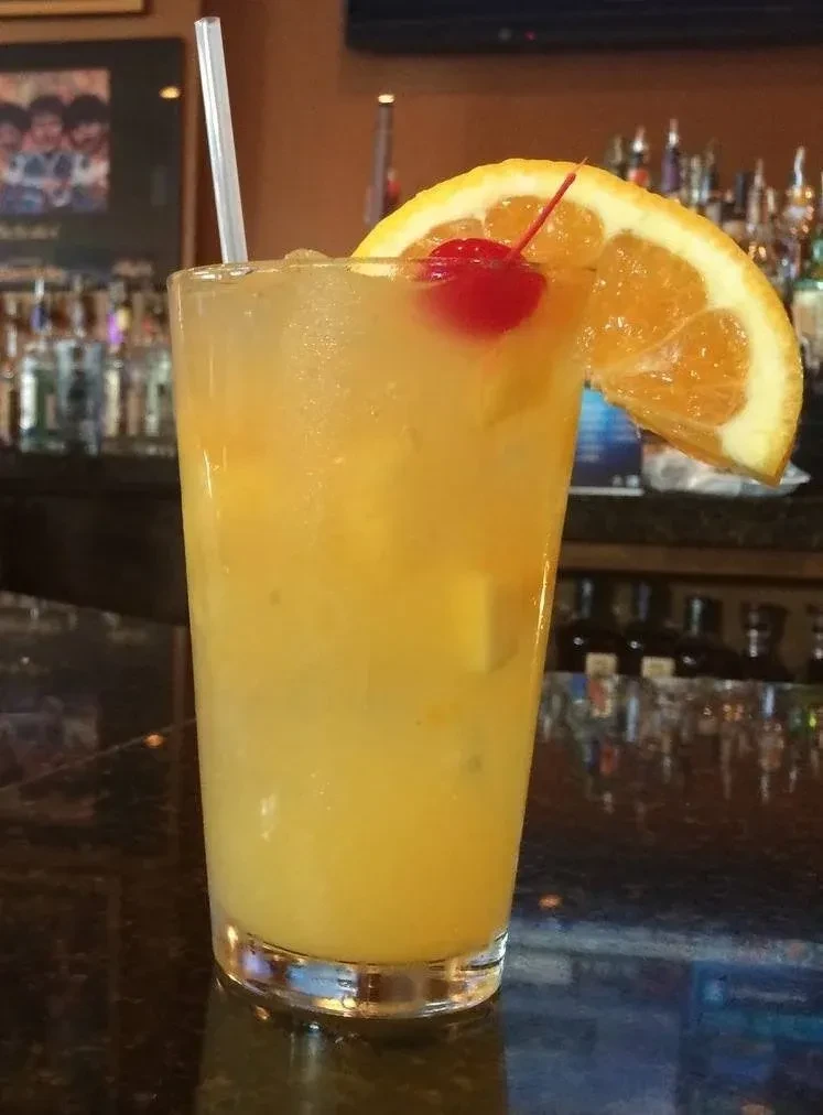 Cold yellowish-orange cocktail with cherry and orange in a bar.