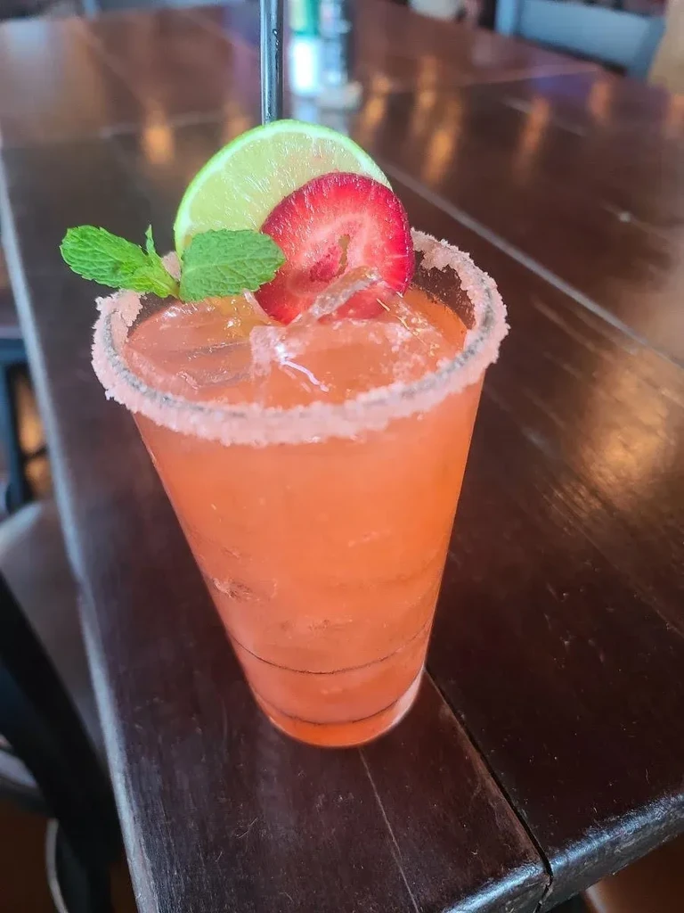 Pinkish-orange cocktail with lime, strawberry, mint, and sugared rim.