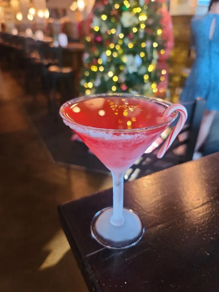 Vibrant frosted red martini with candy cane and glitter, blurred festive background.