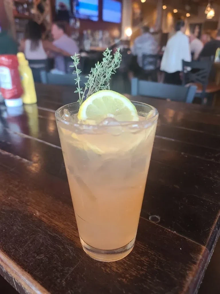 Amber cocktail with ice, lemon, and herb garnish on wood.
