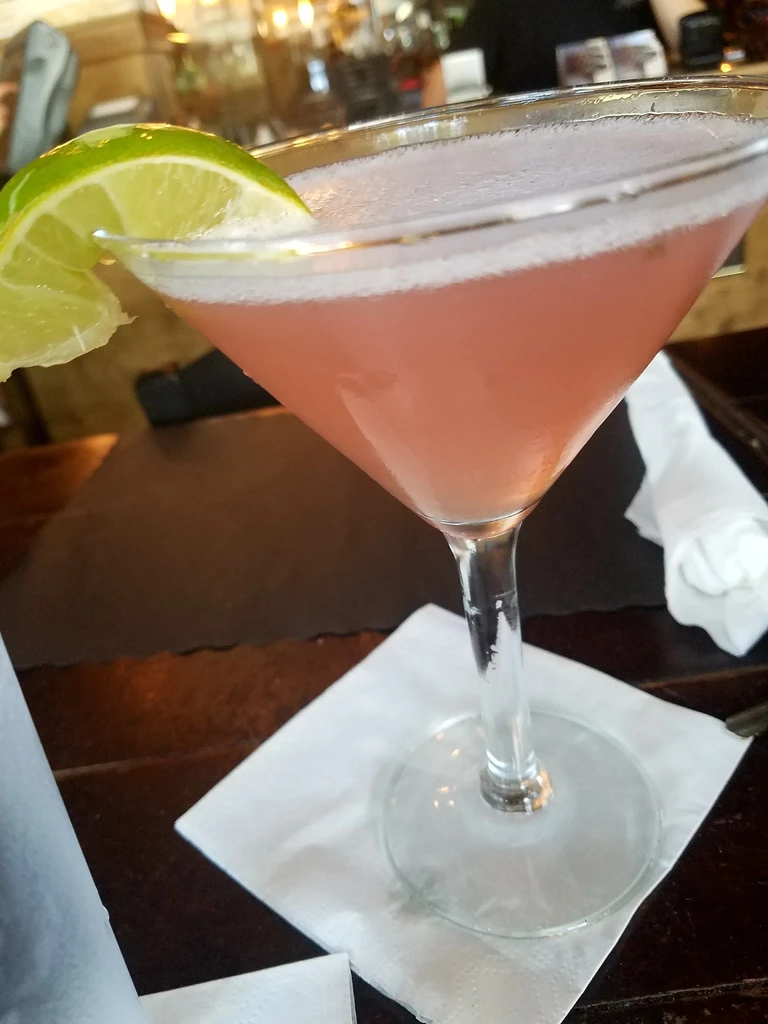 Pink cocktail in martini glass with green lime wedge.