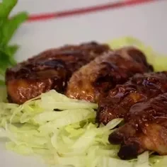 Four glazed meat pieces with dark sauce on shredded lettuce.