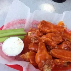 Red basket brimming with orange buffalo wings, celery, and creamy dipping sauce.