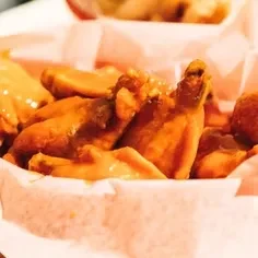 Close-up of glossy, sauced chicken wings in a checkered paper-lined basket.
