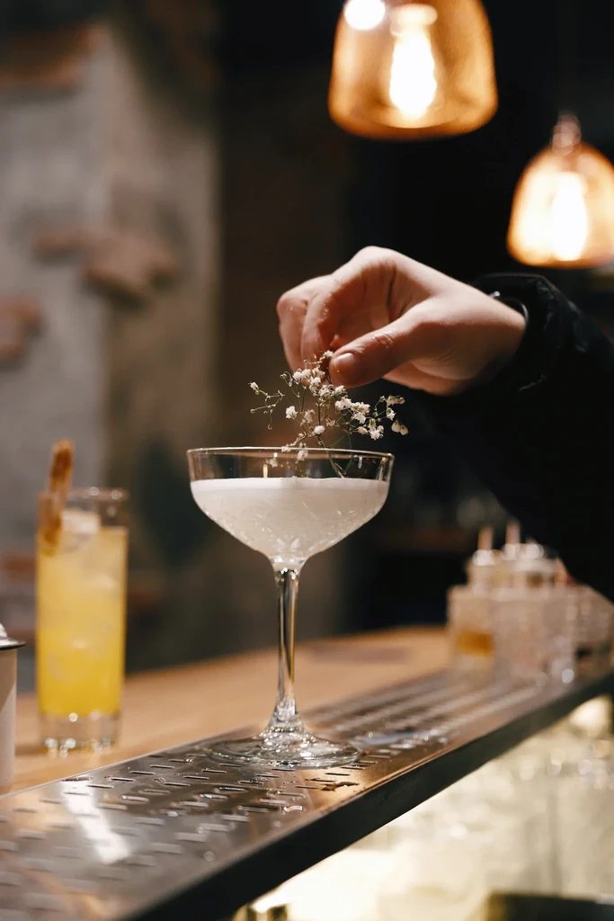 Hand garnishes a milky-white cocktail with small white flowers.
