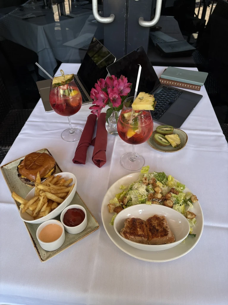 Patio table with two red cocktails, cheeseburger, fries, and Caesar salad.