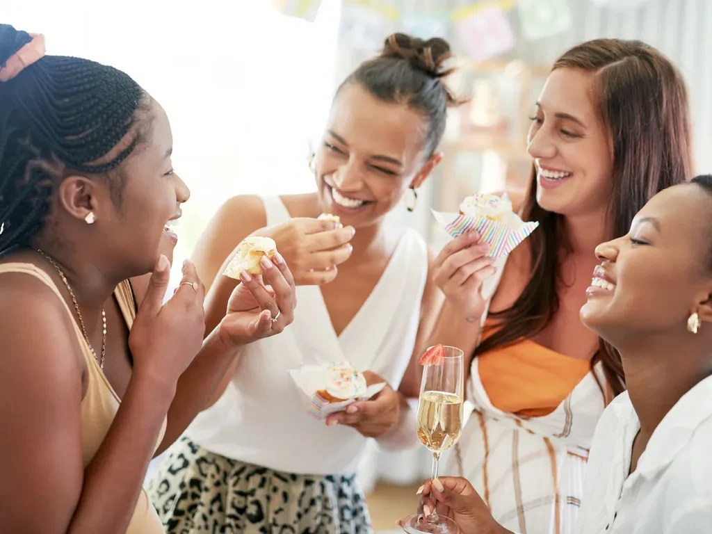 Close-up of four women smiling with cupcakes and champagne.