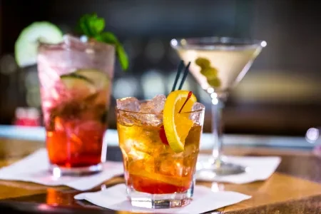 Three unique cocktails with garnishes displayed on a bar counter.
