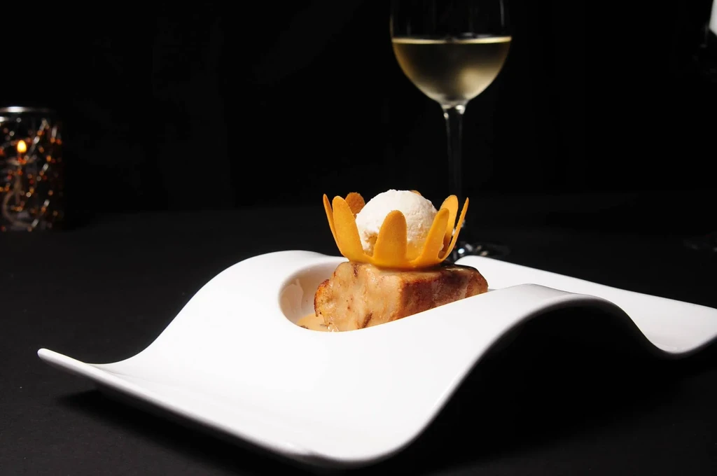Plated dessert with flower-garnished ice cream, wine, and glowing candle.