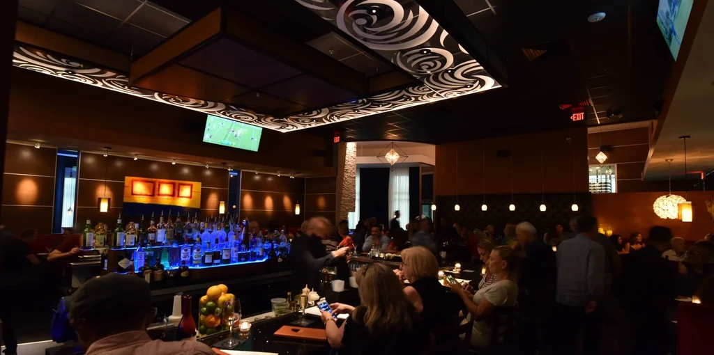 Low-light upscale bar interior with blue-backlit bar and busy diners.