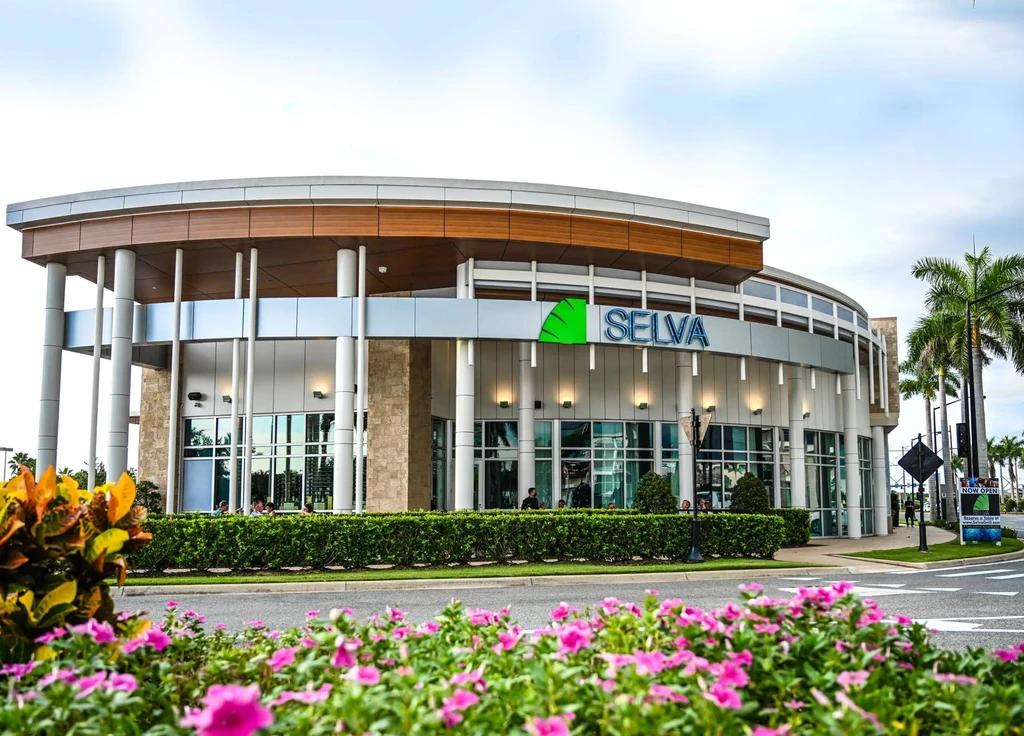Modern circular SELVA restaurant building, large windows, flowers, palm trees.