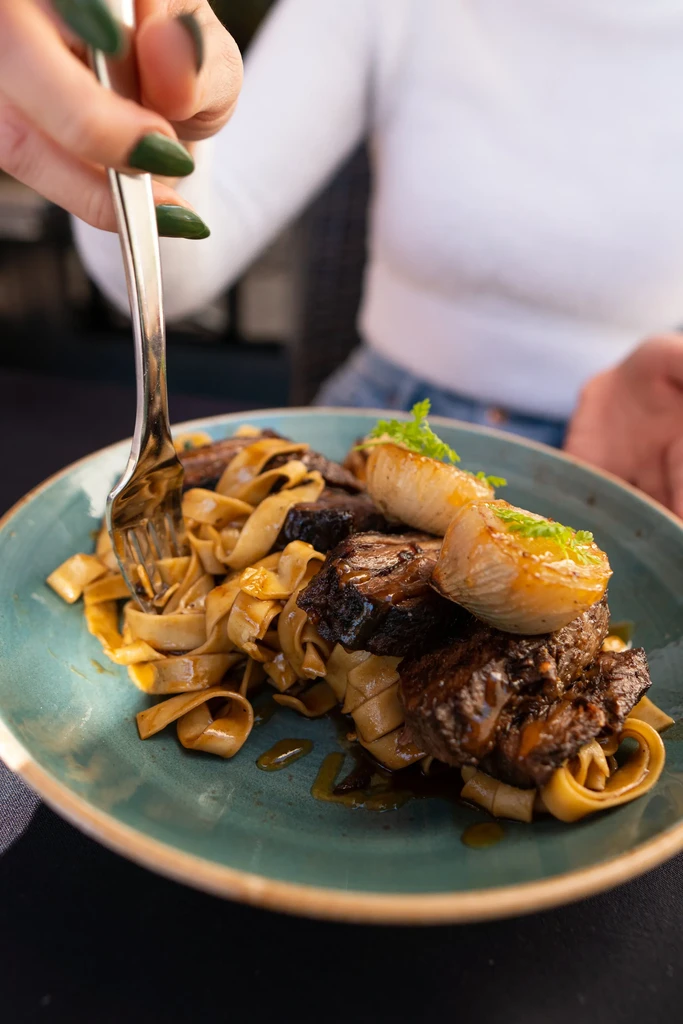 Gourmet pasta with braised meat in a teal bowl, being eaten.