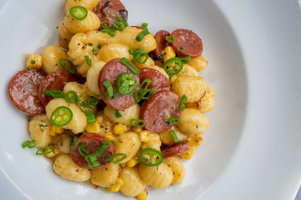 Gnocchi, sausage, corn, jalapeños, and green onions in white bowl.