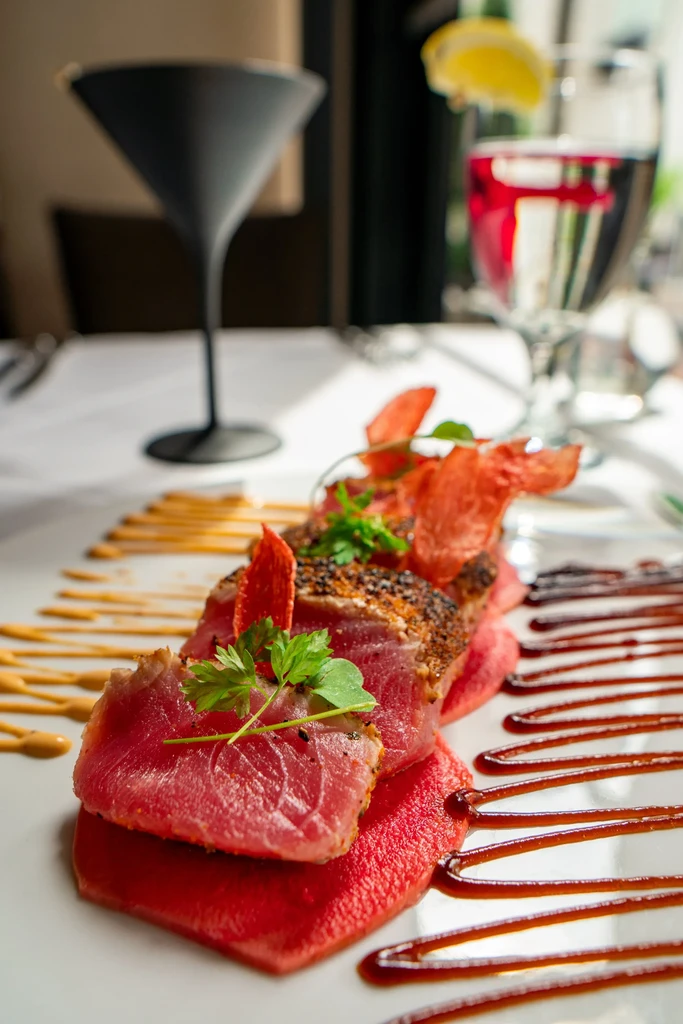 Elegantly plated seared tuna on fruit with sauces, herbs, and drinks.