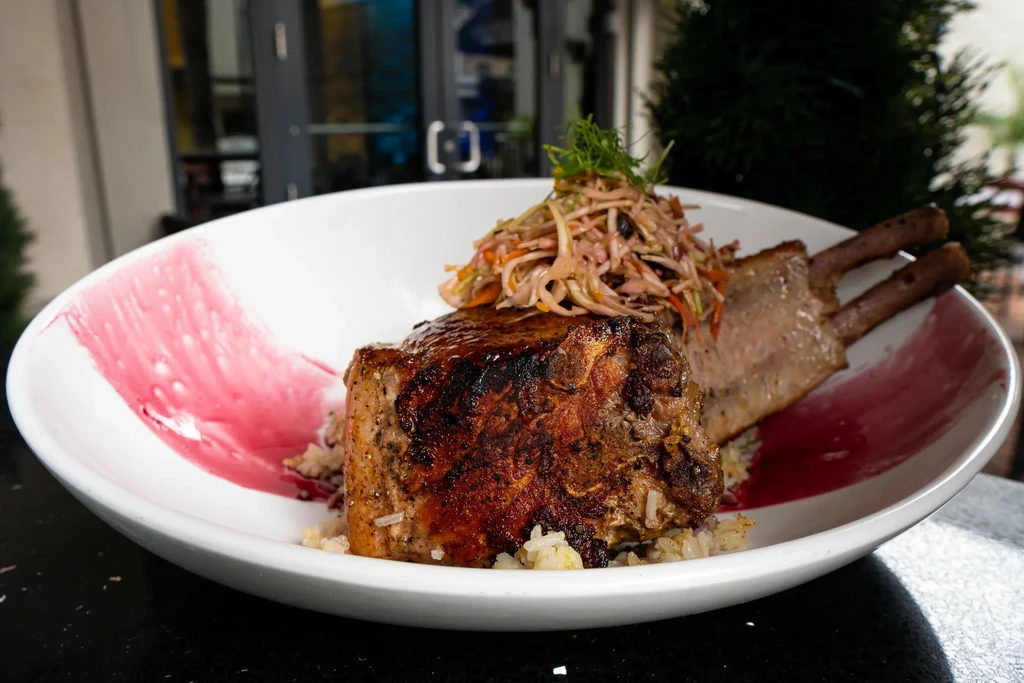 Bone-in seared pork chop on rice with vibrant slaw and sauce.