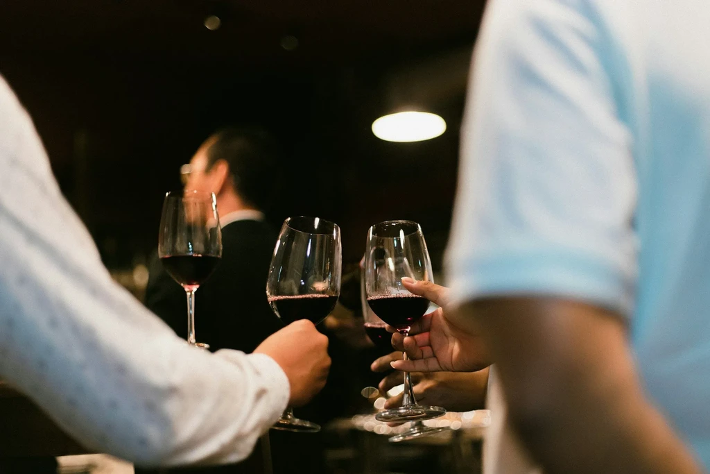 Multiple hands holding red wine glasses in a warm, intimate setting.