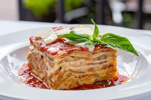 Plated slice of layered lasagna with meat sauce, cheese, and basil.