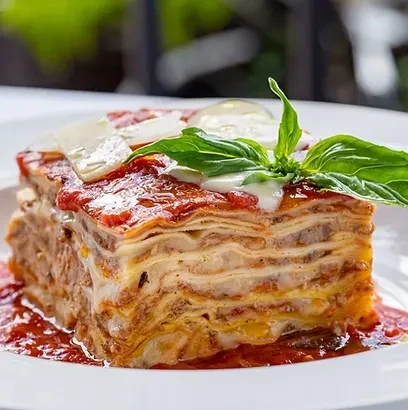 Layered lasagna slice with meat, cheese, tomato sauce, basil, Parmesan.