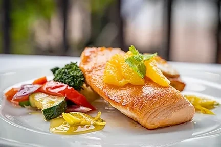 Golden-brown salmon with orange, mint, and sautéed vegetables on a white plate.