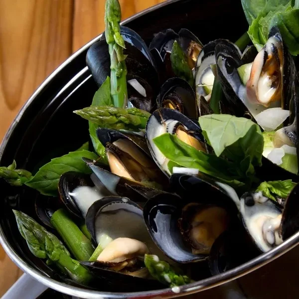 Steamed mussels, green asparagus, basil, creamy sauce in a dark pot.