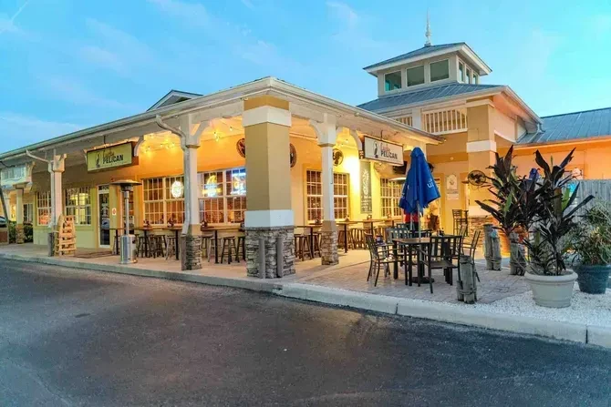 Gulfpelican restaurant exterior at dusk, warmly lit patio with seating.