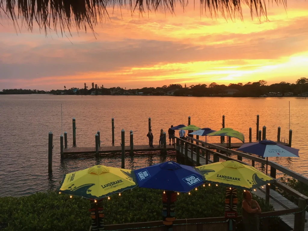 Sunset over water with restaurant patio, dock, and branded umbrellas.