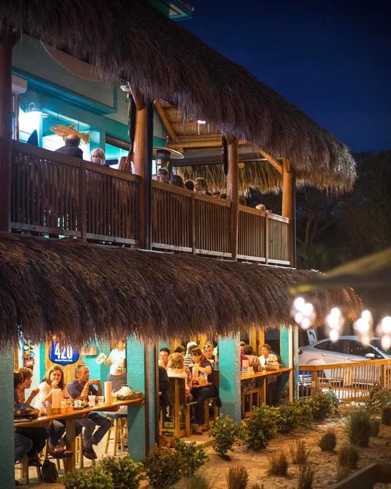 A multi-level tiki-style bar at night, bustling with patrons.