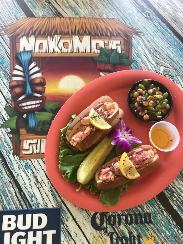 Two lobster rolls, sides, and orchid on a painted wooden table.