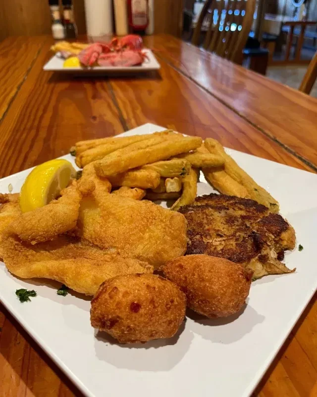 Fried fish, fries, hush puppies, and crab cake on a plate.