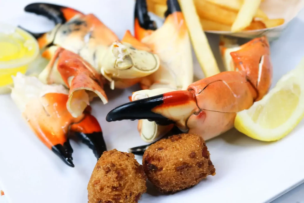 Close-up of cooked crab claws, hushpuppies, butter, and a lemon wedge.